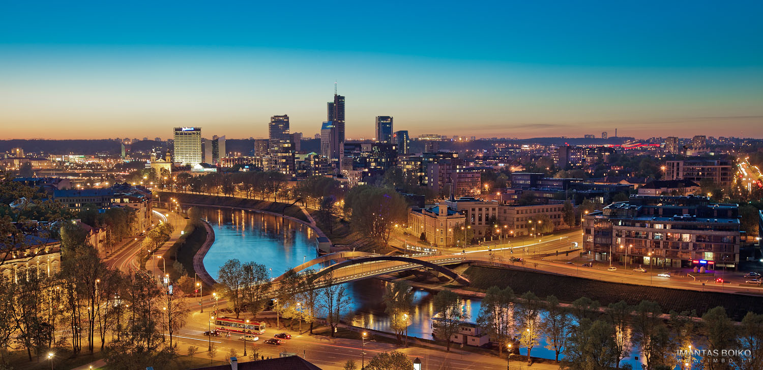 City skyline at dusk, featuring illuminated buildings reflected in a calm river below