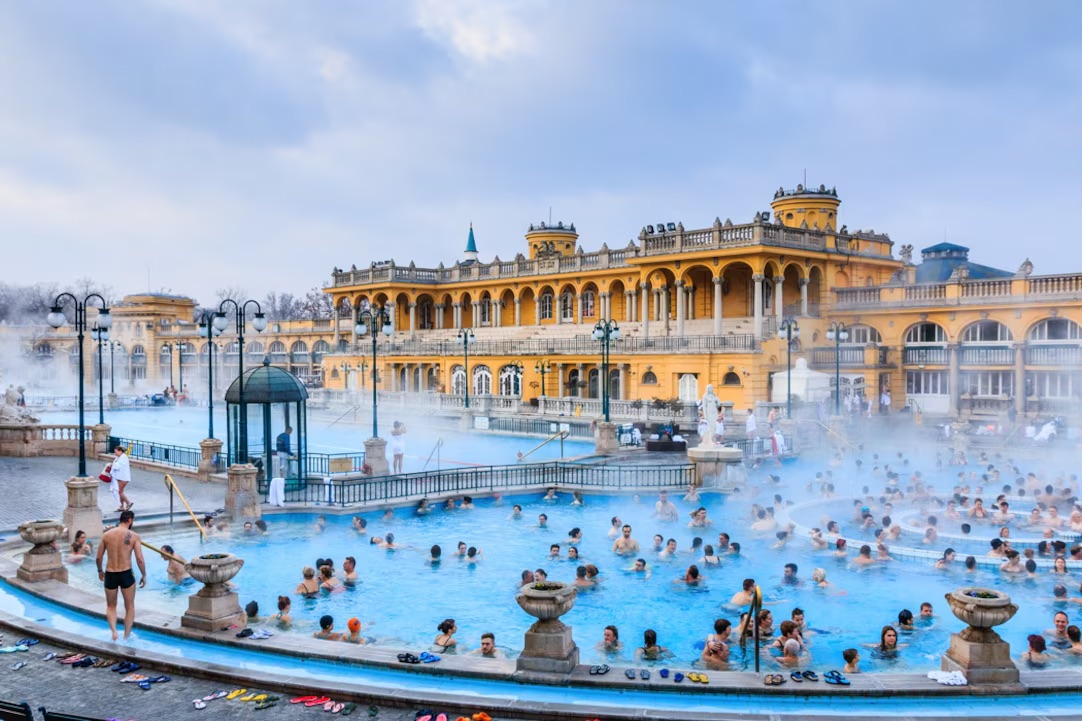 A view of Budapest's renowned thermal baths, featuring historic buildings and people enjoying the warm mineral waters