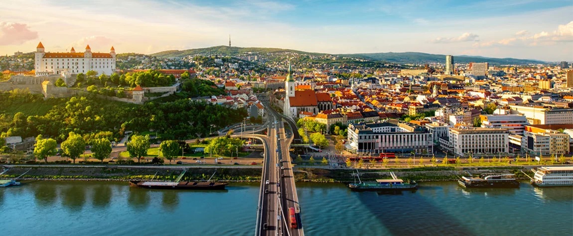 The image is an aerial view of Bratislava, the capital city of Slovakia, with the Danube River in the foreground